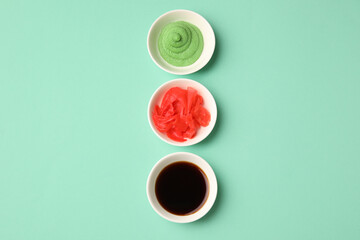 Bowls with wasabi, soy sauce and pickled ginger on turquoise background