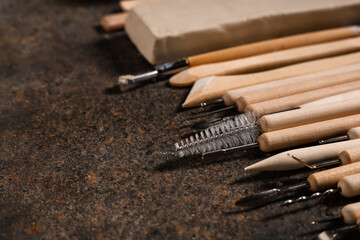 Set of sculptor tools with clay on black grunge table, closeup