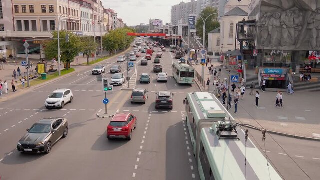 Minsk, Belarus - July 13, 2024: car traffic and pedestrians moving along a busy alley in a European city showing cars, trolleybuses and people crossing an intersection on a sunny day