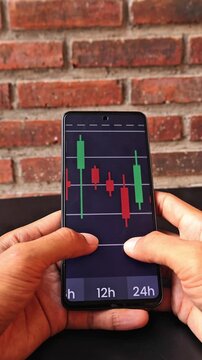 Hands are scrolling the movement of digital stock charts on a cell phone
