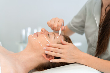 Dermatologist applying cream on the face of a woman lying on bed. Young lady receiving a skincare procedure in a beauty salon, enjoying a relaxing treatment 