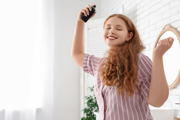 Naklejka premium Happy young redhead woman applying hair spray in bathroom