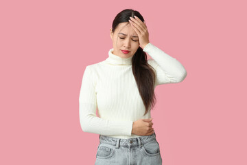 Young Asian woman suffering from headache on pink background. Brain Injury Awareness Month