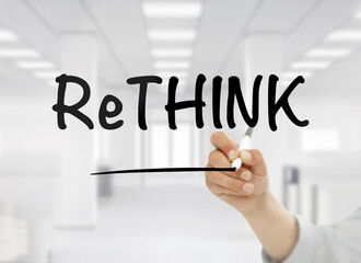 A conceptual business image showing "ReThink" handwritten in bold black letters on transparent glass, with a blurred modern white office interior in the background. 