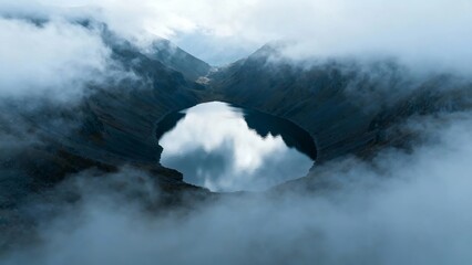 Aerial view of a mountain crater lake surrounded by clouds and mist