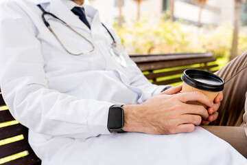 Healthcare professional taking a moment to relax outdoors, holding a paper coffee cup while sitting on a park bench, enjoying a brief respite from work. Unrecognizable person