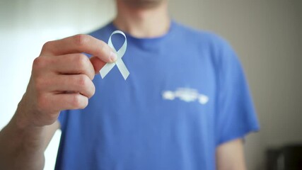 A young man holds a blue satin ribbon, symbol for Prostate Cancer Awareness Month in November. Concept of diagnosis, treatment, and community support.