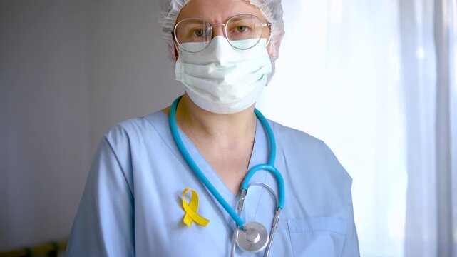 A woman medical staff holds a yellow satin ribbon, emblem for sarcoma, childhood cancer, suicide prevention, endometriosis and liver disease awareness.