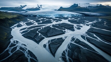 Aerial view of glacial river meandering across black sand, backed by icy mountains