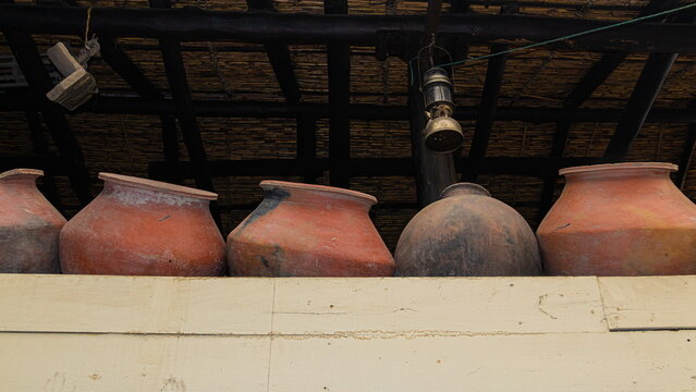 A row of handcrafted clay pots, used for traditional Andean cooking and water storage, are stored on a shelf under a canopy.