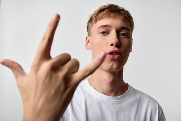 Hand gesture, rock on, young man, white t shirt, facial expression, confidence, attitude, lifestyle. Close up scene highlighting bold pose and intense gaze suitable for music, youth culture and