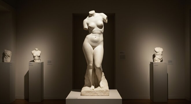 Center headless female statue stands on pedestal Left  right smaller torso statues each on tall stands
