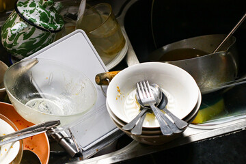 A pile of dirty dishes stacked in a kitchen sink with bowls, plates, spoons, and cups waiting to be...