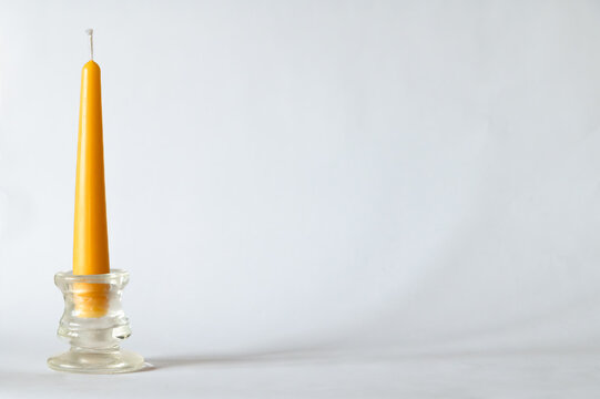 A single yellow beeswax taper candle in a glass candlestick holder on white background, copy space on right
