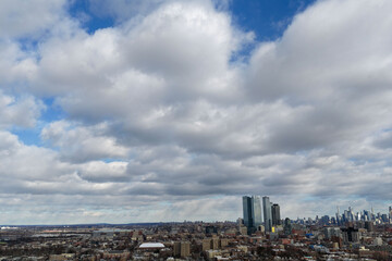 Aerial drone photo from Jersey City featuring Manhattan skyline views, dense city blocks, waterfront buildings, and modern New York City architecture under dynamic daytime cloud cover.                