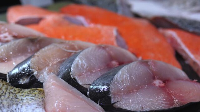 Close up view of fresh raw fish for sale at a seafood market, featuring various types of fish fillets and steaks neatly arranged, highlighting the freshness and quality of the catch