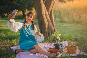 Fototapeta premium Young Latina woman enjoying a picnic in the park using her cell phone.