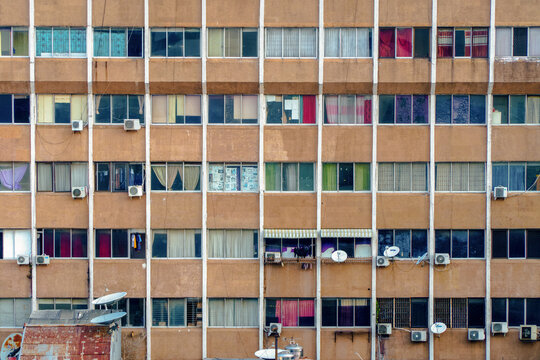 Old apartment with colorful curtains in Jakarta, each window hinting at the harsh yet vibrant life of the city's crowded streets.
