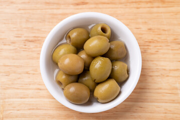 Pickled olives, Pitted green olives in a bowl on wooden background, Table top view