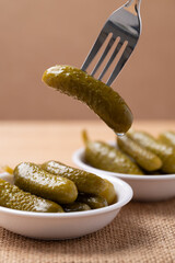 Pickled cucumber or Gherkin pickle in a bowl with fork on brown background