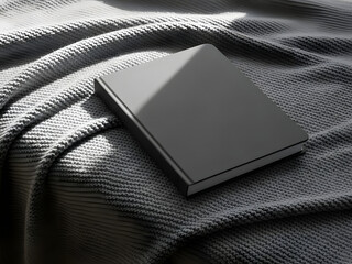 Plain closed book on textured fabric surface with sunlight and shadow