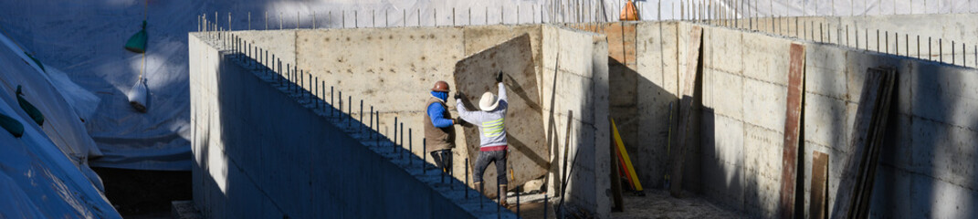 Construction workers removing wood forms from large stormwater retention system tank construction job site, cement foundation and retaining walls poured, sunny fall day
