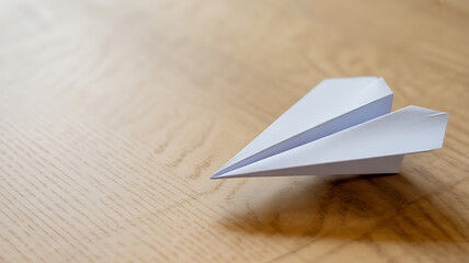 A white paper airplane resting on a wooden surface