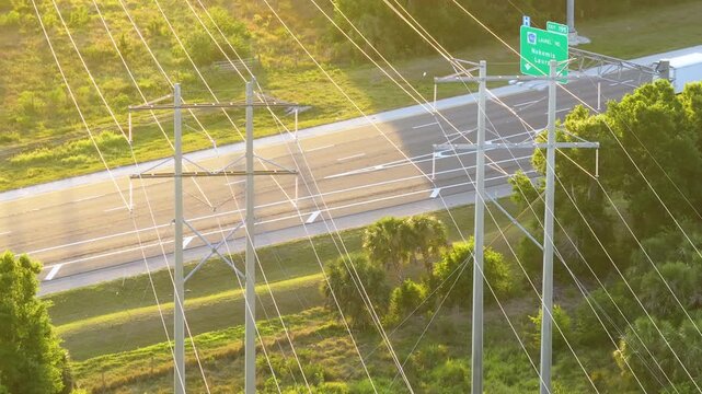 Electrical transmission lines stretch over freeway lanes with traffic below. High voltage towers as part of utility infrastructure