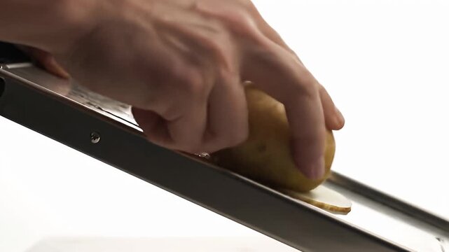 Close up of potato being sliced on a mandoline slicer kitchen preparation