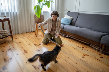 Woman pet caretaker playing with cat on floor at home. Female stimulating hunter instincts with pole toy, fun with kitten, joyful activity, domestic feline and pet sitter fun, behavior encouragement