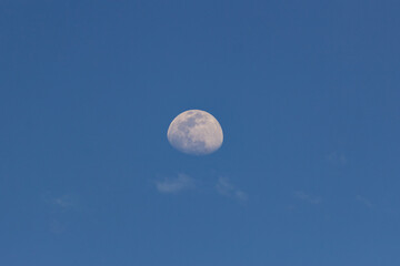 Moon in the blue sky with white clouds. Blue sky background.