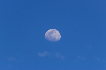 Moon in the blue sky with white clouds. Blue sky background.