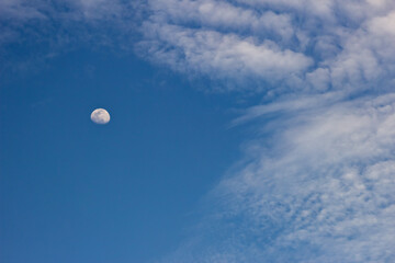 Moon in the blue sky with white clouds. Blue sky background.