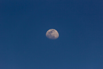 Moon in the blue sky with white clouds. Blue sky background.
