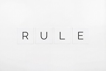 Minimalist flat lay of the word rule spelled on white square cards over white background