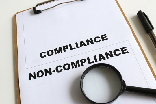 Compliance and non compliance text on paper with magnifying glass and a pen with isolated white background. Audit result. Business and financial concept for improvement with implementation of audit.