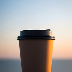 A brown disposable coffee cup with a black lid against a sunset background