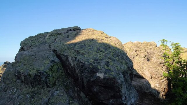 A scenic view of a rocky mountain peak in the Southern Urals, Russia, with clear blue skies and natural light. The remote wilderness of Taganai National Park offers stunning natural beauty and hiking 