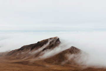 Rugged mountain peaks rise above a blanket of fog, creating a tranquil atmosphere amid the cool afternoon. Nature exhibits breathtaking beauty. Generative AI.