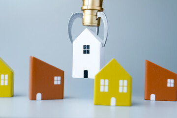 A claw machine lifting a small house model among other houses. House hunting, mortgage selection, choosing a home concept.