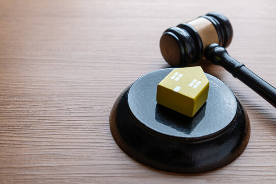 A small yellow house model and a judge's gavel. Real estate law, property rights, foreclosure concept.