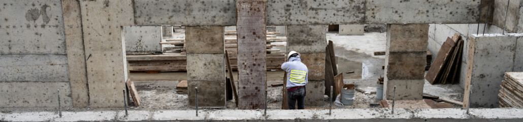 Construction worker using hammer to remove wood form from pored cement wall in a large stormwater retention system tank on a construction job site, sunny fall day
