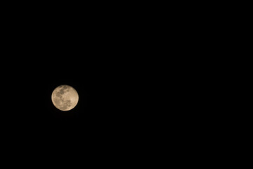 Horizontal photo of full moon. Moon with nice soft yellow color. Visible craters on the edge of space body. The bright and light areas on surface are clearly visible. Space around is black.