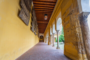 A long arched walkway with yellow walls, wooden ceiling, hanging lanterns, and ancient stone columns leads toward the courtyard at the Mezquita-Cathedral in Cordoba Spain during spring dusk.