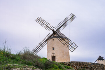 A traditional stone windmill stands on a grassy hill in Consuegra, Spain, famous as the site of Don Quixote battle in La Mancha.
