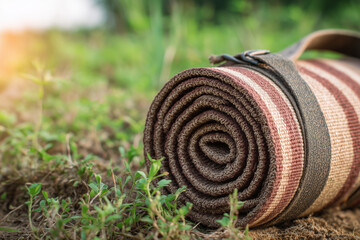 Rolled up yoga mat on grass with sunny outdoor background