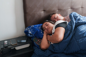 Couple resting comfortably in bed with an alarm clock set for 8:00 am