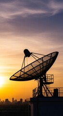 Satellite dish silhouetted against a vibrant sunset sky above a cityscape. Telecommunication and broadcasting concept for global connection.