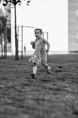 Young girl with a teddy bear running joyfully across a grassy field, wearing a light dress and sneakers, capturing the essence of childhood playfulness and freedom