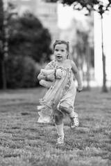Young girl with a teddy bear running joyfully across a grassy field, wearing a light dress and sneakers, capturing the essence of childhood playfulness and freedom